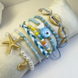 Detalle de tobilleras bohemias con cuentas, conchas y estrellas de mar en un soporte