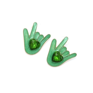Détail macro de boucles d'oreilles geste de la main avec émail vert et gemme cœur