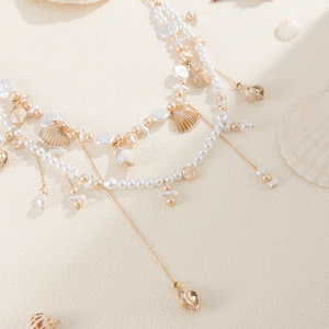 Detail view of multi-layer pearl waist chain with golden shells on sandy beach background