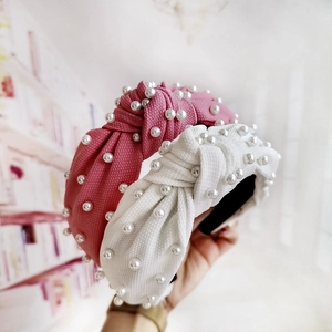 Detail of hand-held knotted headbands with white pearls on pink and white fabric