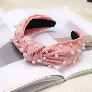 Detail of pink knotted fabric headband with white imitation pearls on a white magazine