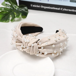 Detail of beige knotted fabric headband with white pearls on a minimalist background