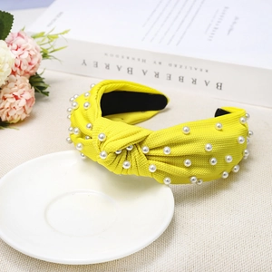 Close-up of bright yellow knotted headband with faux pearls on textured fabric