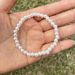 Close-up of white round faux pearl bracelet for girls on outdoor grass background