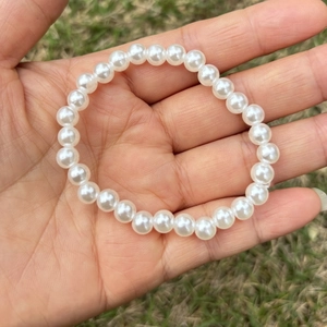 Close-up of a white imitation pearl elastic bracelet for girls held over a green lawn