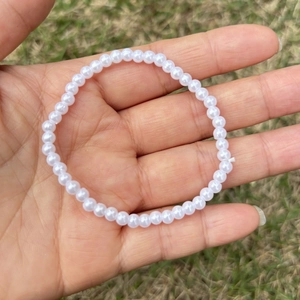 Detailed view of elastic white faux pearl beaded bracelet on hand with outdoor background