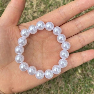 Close-up of a white imitation pearl bracelet for girls held over a green grass background