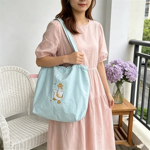 Detail of light blue canvas tote bag with happy duck embroidery and drawstring closure