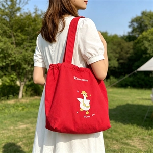 Red canvas tote bag with cute cartoon duck embroidery and crown logo in outdoor setting