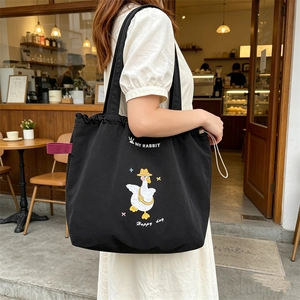 Detail of cute duck embroidery and drawstring closure on a black canvas tote bag