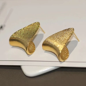Macro detail of gold triangular stud earrings featuring a textured grid surface finish