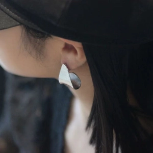 Macro view of silver triangular earrings with brushed metal texture worn by a model