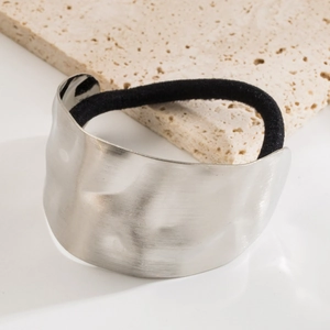 Minimalist silver metal hair tie with textured finish on a neutral stone background
