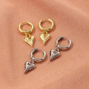 Detail of gold and silver stainless steel heart hoop earrings on rose gold satin fabric