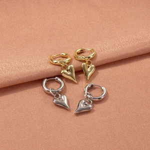Detailed view of polished gold and silver heart dangle earrings on pink satin fabric