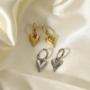 Polished gold and silver heart drop earrings displayed on a soft beige silk background