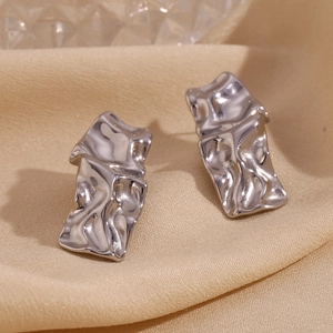 Détail de boucles d'oreilles rectangulaires argentées avec texture plissée sur satin champagne