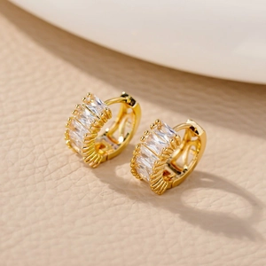 Macro view of gold hoop earrings with baguette-cut zircon stones and beaded metal edges