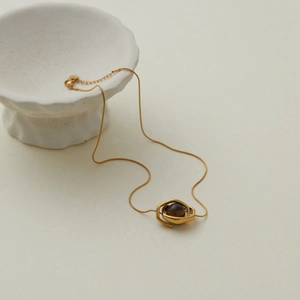 Detailed view of a gold stainless steel necklace with tiger eye stone on ceramic prop