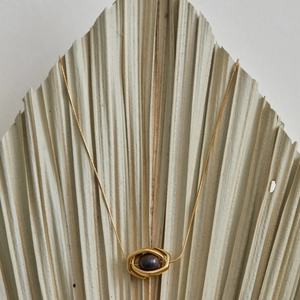 Gold stainless steel necklace with geometric pendant and tiger eye stone on palm leaf