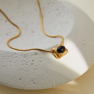 Detailed macro of gold square pendant with black oval gemstone on flat snake chain