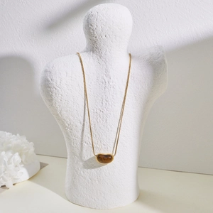 Detailed view of a gold bean-shaped necklace with tiger eye stone on a white mannequin