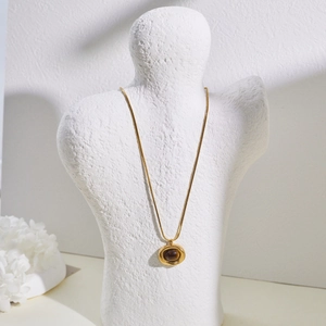 Close-up of gold snake chain necklace with oval tiger eye stone on a white mannequin