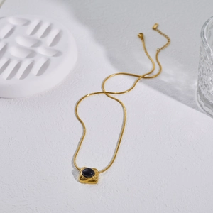 Detailed macro view of gold snake chain necklace featuring a vintage square gemstone pendant
