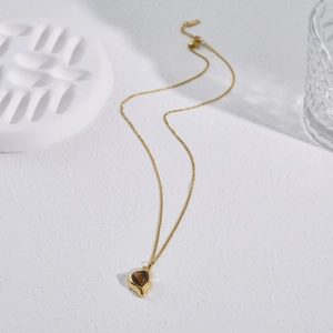 Detail of gold geometric necklace with tiger eye stone on white textured background