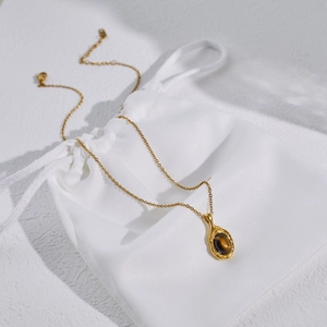 Detail of tiger eye stone necklace with gold lava texture pendant on a white fabric pouch