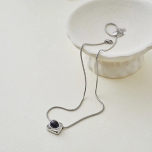 Detail view of a square pendant with black oval stone on a silver snake bone chain