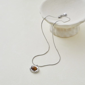 Detail of silver snake chain with geometric pendant featuring natural tiger eye stone
