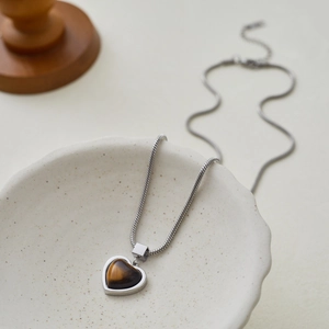 Detail of heart-shaped tiger eye stone pendant with sleek silver snake chain on ceramic