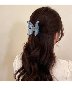 Blue acetate butterfly hair claw clip with pearlescent texture worn on long wavy hair
