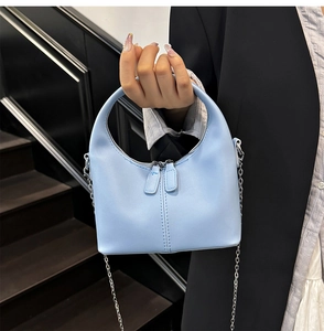 Détail d'un sac à main en cuir souple bleu clair avec chaîne argentée et zips
