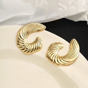 Detail of vintage golden C-shape swirl earrings with ribbed texture on porcelain plate