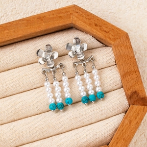 Detail view of pearl tassels and turquoise beads on butterfly earrings in a wooden box