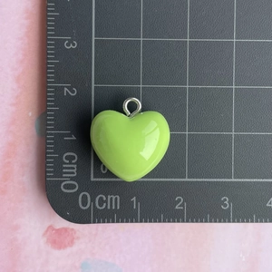 Macro shot of 1.5cm green resin heart charm with silver ring on black grid mat