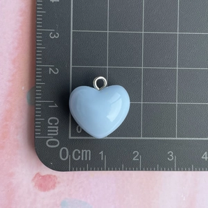 Detail view of a 1.5cm light blue resin heart pendant with silver loop on a scale mat