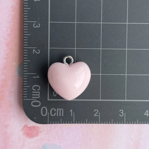 Pink heart resin pendant with silver ring shown on a metric measurement scale mat