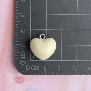 Detailed size view of cream resin heart pendant with silver metal ring on a grid scale