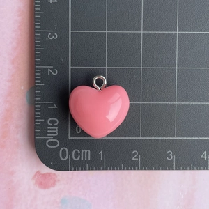 Detail shot of a 1.5cm pink resin heart pendant with silver loop on a scale ruler