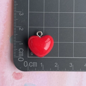 Macro view of 1.5cm red resin heart pendant with silver ring on measurement grid