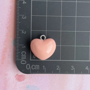 Macro view of a 1.5cm pink resin heart pendant with silver ring on a scale mat