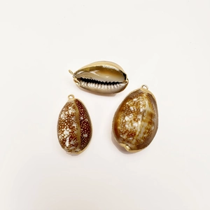 Macro shot of three natural cowrie shell pendants with gold plated edges and top jump rings