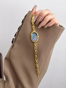 Detail of vintage gold chain watch featuring an oval blue dial on a stylish blazer sleeve