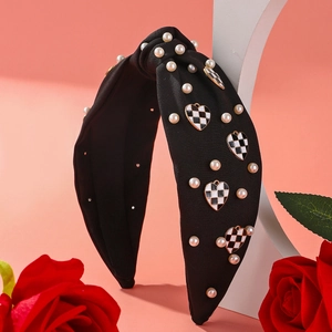 Detail of black fabric headband with pearls and checkered heart charms on a stand