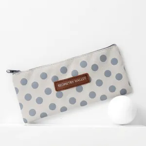 Minimalist canvas pencil case with blue polka dots and leather label on white pedestal