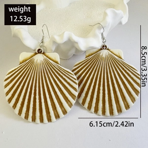 Detailed view of oversized scallop shell earrings with brown stripes on sand background