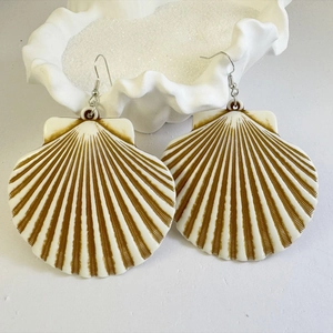 Macro detail of striped scallop shell earrings on white sand beach background